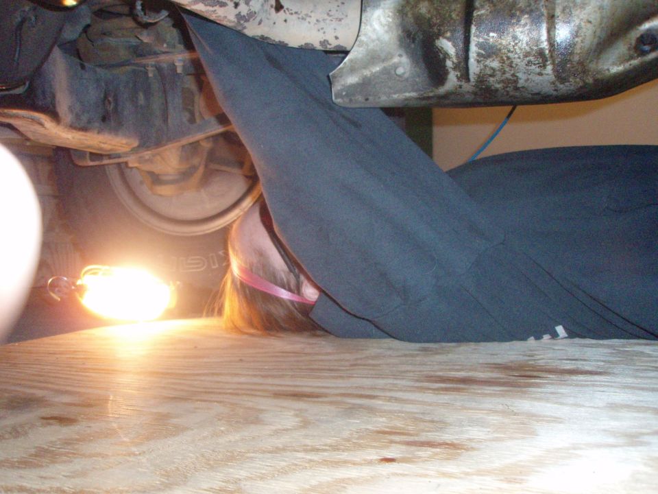 Person working under a vehicle with a light illuminating the underside