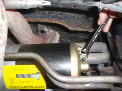 1987 Ford Bronco - A wrench is used to secure a starter motor, with a yellow tag providing installation instructions.