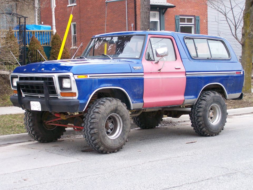 Blue Ford Bronco with a pink door, lifted with large tires