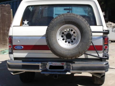 1989 Ford Bronco - Straight-on rear view of a white full-size Ford Bronco with a red and gray bodyside stripe, a blue Ford oval on the tailgate and a Dallas C…