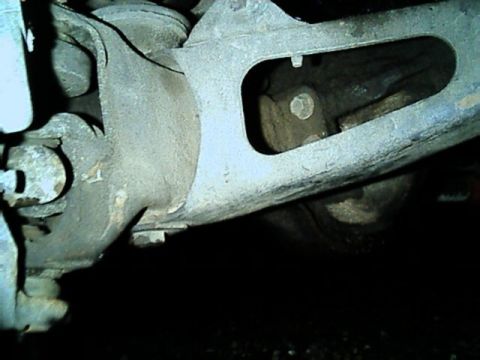 1989 Ford Bronco - Underbody close-up of a cast radius arm bolted to the front axle housing, with its oval lightening window, mounting bolt heads and the axle…