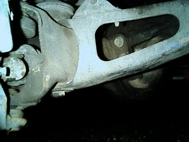 Cast radius arm bolted to a front axle housing, viewed from underneath and coated in dirt