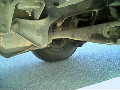1989 Ford Bronco - Underbody view of a truck's front suspension shot from ground level, showing the radius arm running rearward from the axle to its frame-sid…