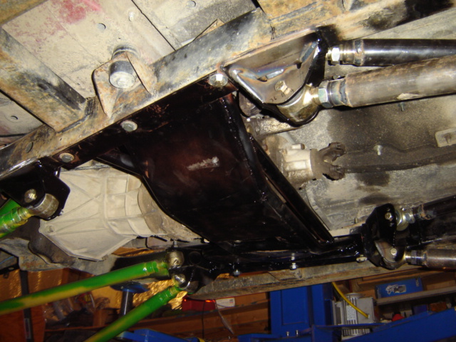 Vehicle undercarriage with black painted frame components, green suspension arms, and a transmission