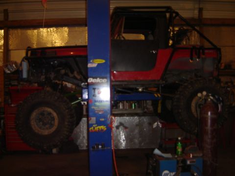 1992 Ford Bronco - Modified off-road vehicle with a roll cage is elevated on a shop lift, showing its large tires and construction.