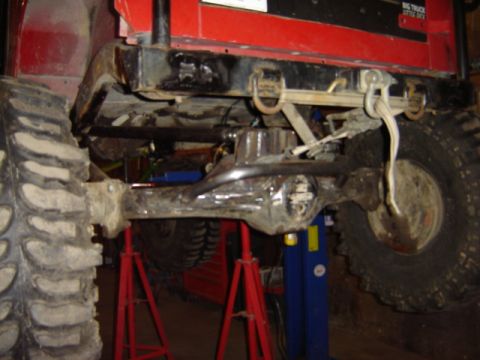 1992 Ford Bronco - The underside of a heavily modified off-road vehicle, showing its rear axle and large tires.