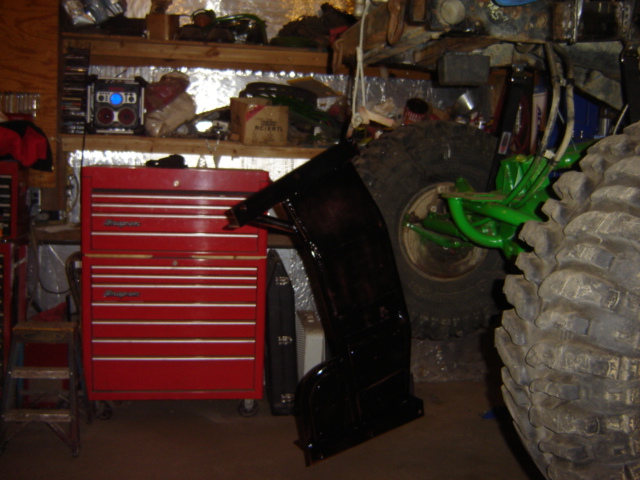 Black vehicle part next to red toolbox with large tires and green suspension
