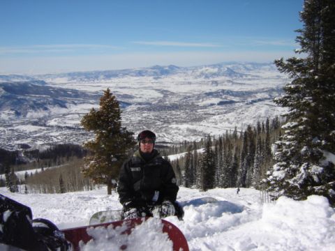 1992 Ford Bronco - A snowboarder takes a break on a snowy mountain slope, with a vast valley and distant mountains visible.