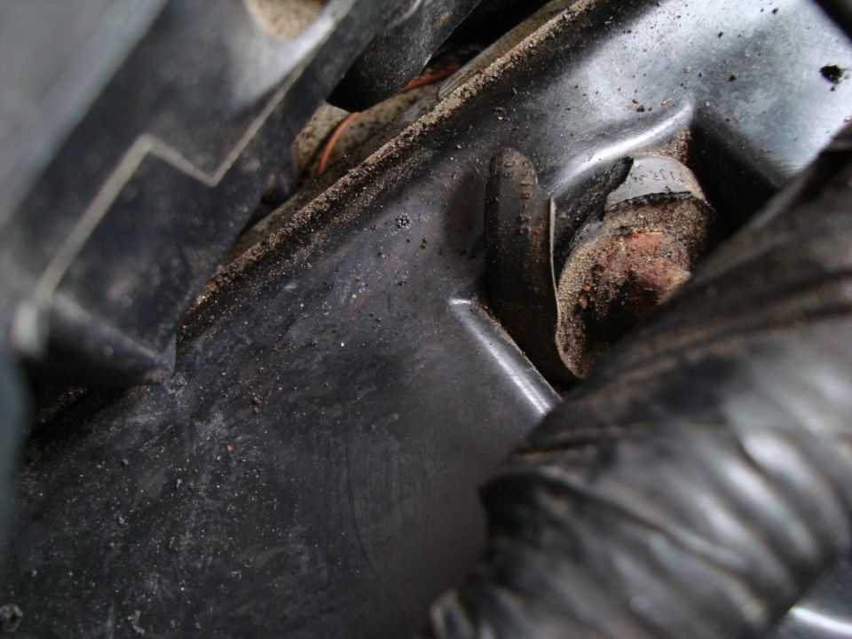Close-up of a dirty engine bay bracket and bolt in a vehicle