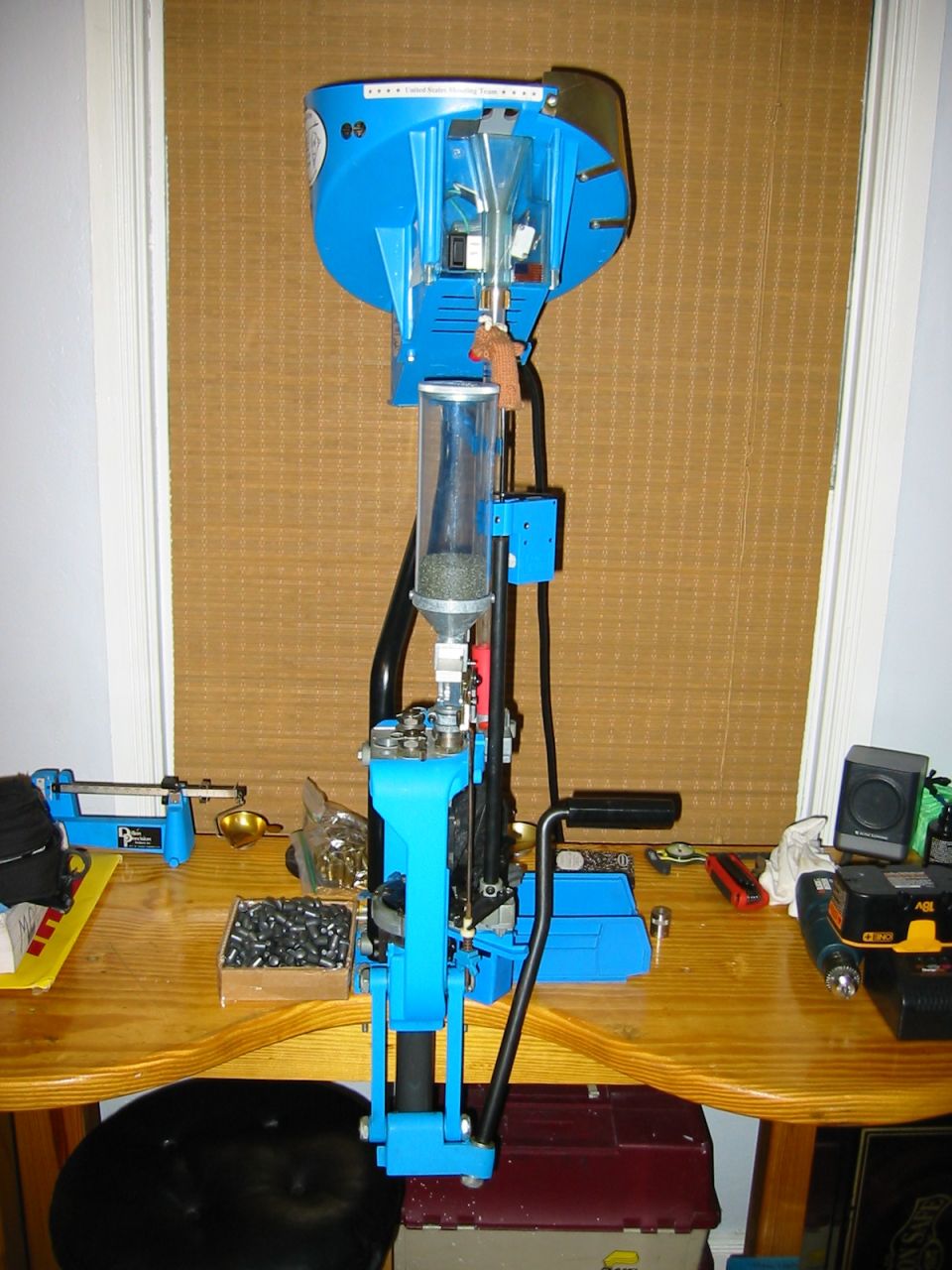 Blue reloading press on a wooden table with ammunition components