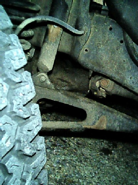 1989 Ford Bronco - Under-vehicle shot of a front suspension shock mount and radius arm, with a rusty forged arm running from the axle bracket toward the frame…