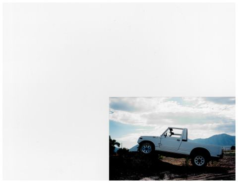 1988 Suzuki Samurai - A white pickup truck is parked on a dirt incline under a cloudy sky with mountains in the distance.