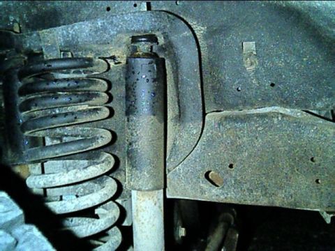 1989 Ford Bronco - Close-up view of the front suspension's coil spring and shock absorber, showing signs of rust and wear.