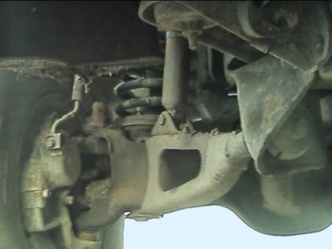 1989 Ford Bronco - Underside view of a solid front drive axle housing with its cast differential and lightening windows, a coil spring on the axle perch, a sh…