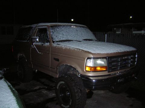 1996 Ford Bronco - A tan 1996 Ford Bronco sits outside covered in snow during the evening.