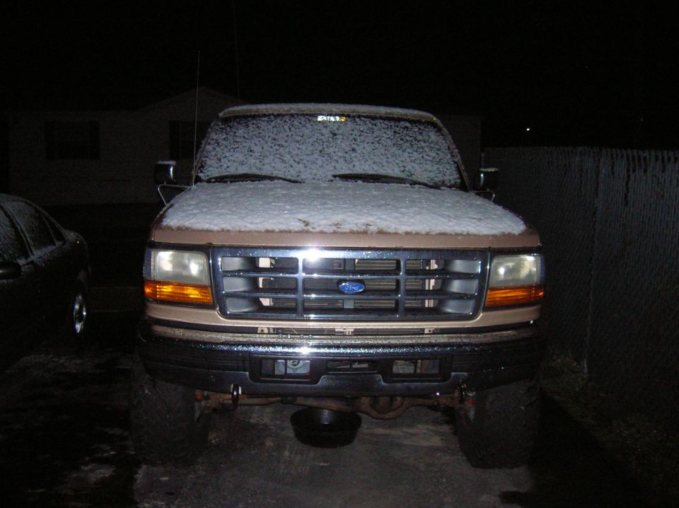 1996 Ford Bronco front end covered in snow, parked at night