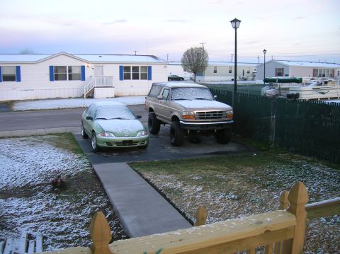 1996 Ford Bronco - Two vehicles sit in a yard dusted with snow, with mobile homes in the background.