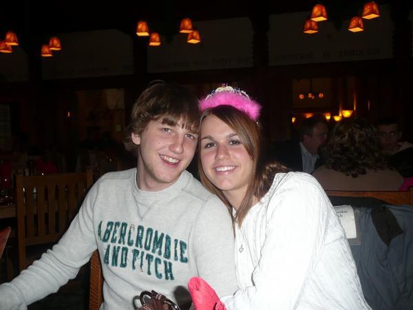 Young couple smiling at a table in a restaurant. Woman wears a pink tiara