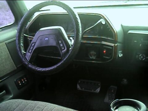 1989 Ford Bronco - Driver's-side dashboard view of a Ford truck with a wrapped steering wheel over the Ford-badged column, cruise buttons on the wheel spokes,…