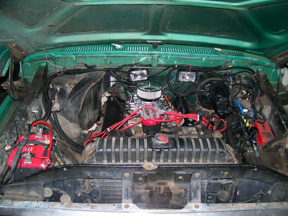 Engine bay of teal 1979 Ford Bronco with V8, chrome air cleaner, red plug wires, and red battery
