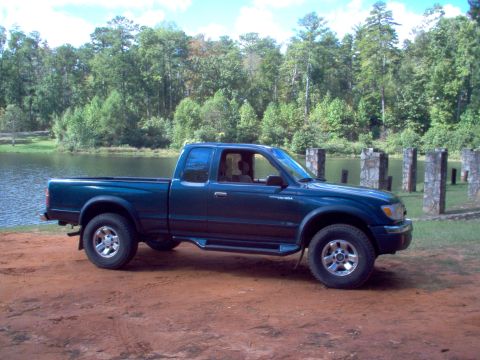 1998 Toyota Tacoma - A 1998 Toyota Tacoma is parked near a body of water with a wooded area behind it.
