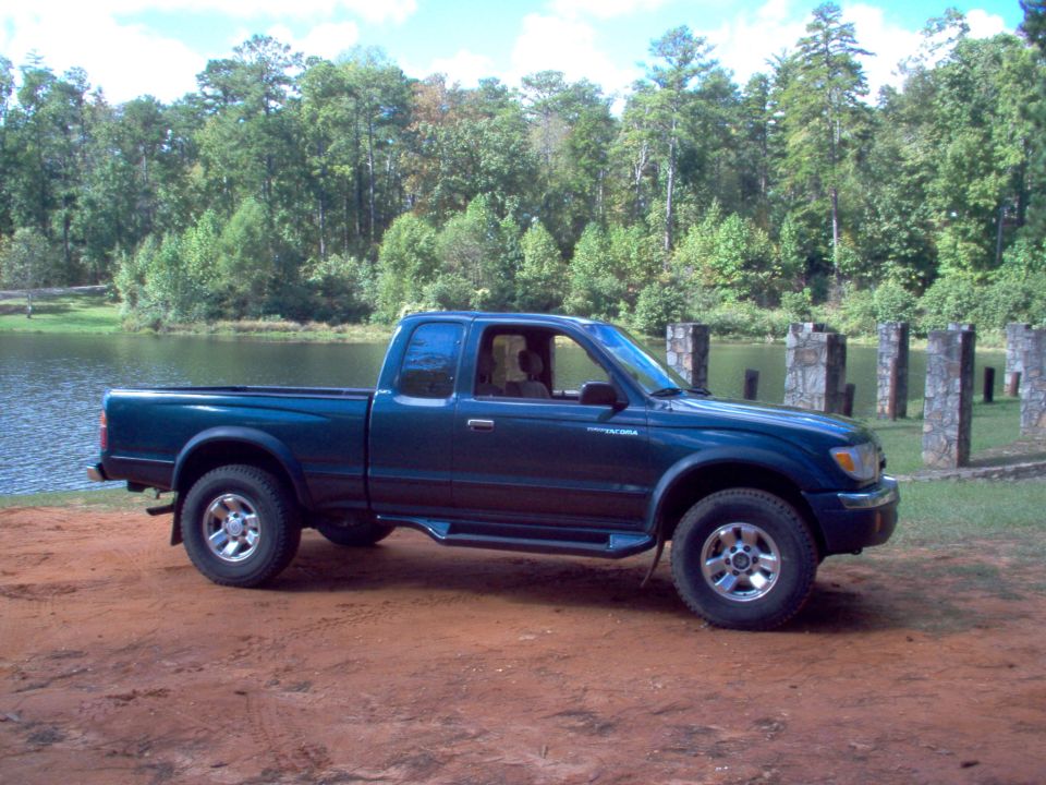 Dark blue 1998 Toyota Tacoma parked by a lake with trees in the background