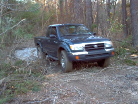 1998 Toyota Tacoma - A dark blue 1998 Toyota Tacoma navigates a muddy, wooded trail.