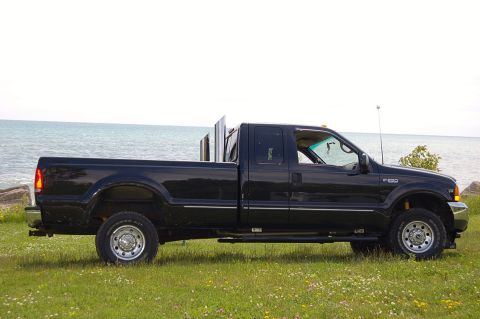 1979 Ford Bronco - This black Ford F-250 pickup truck is parked by the water, prominent dual exhaust stacks.