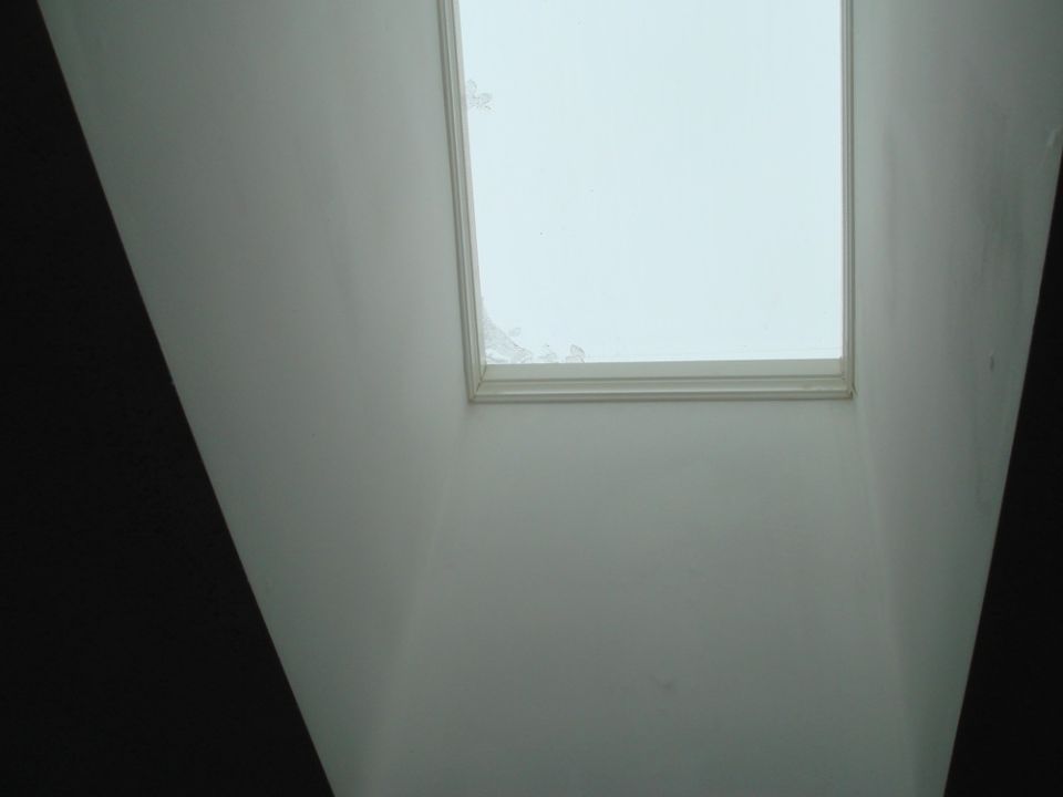 Interior view looking up at a skylight with a white frame and some damage to the glass