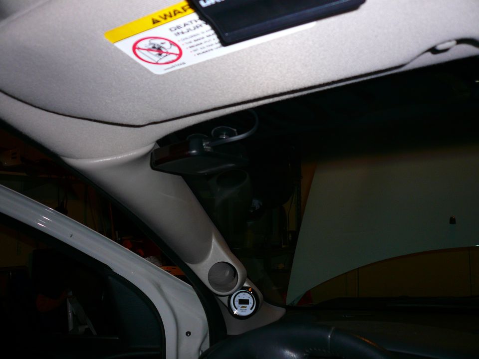 Interior shot of a car showing a gauge pod on the A-pillar with a digital gauge and a warning sticker on the sun visor