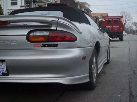 2000 Chevrolet Camaro - Rear view of a silver 2000 Chevrolet Camaro Z28 convertible with a red truck in the background.