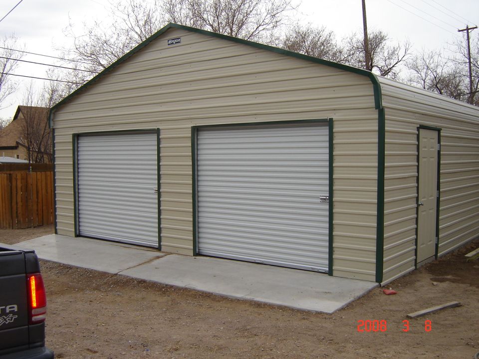 Metal garage with two roll-up doors and a side door. A truck is partially visible in the foreground