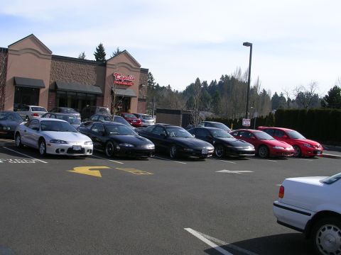 2007 Mazda 3 - A row of cars, mostly Mitsubishi Eclipses, are parked in a lot outside a restaurant.