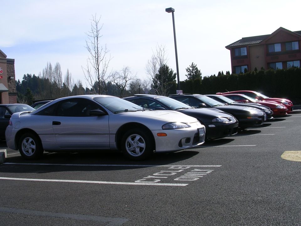 Silver coupe parked in a lot, front 3/4 view. Other cars are lined up behind it