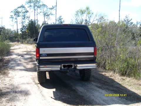 1992 Ford Bronco - Rear view of a 1992 Ford Bronco driving on a dirt road through a wooded area.