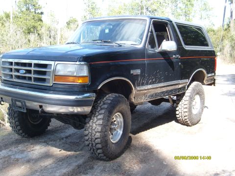 1992 Ford Bronco - A black 1992 Ford Bronco is shown with a lifted suspension and large off-road tires, parked outdoors on a dirt road.
