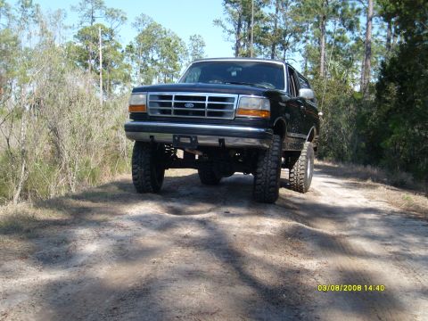 1992 Ford Bronco - Lifted 1992 Ford Bronco driving on a dirt road through a wooded area.
