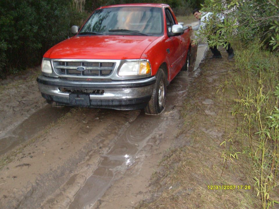 Red Ford F-150 stuck in mud with someone pushing
