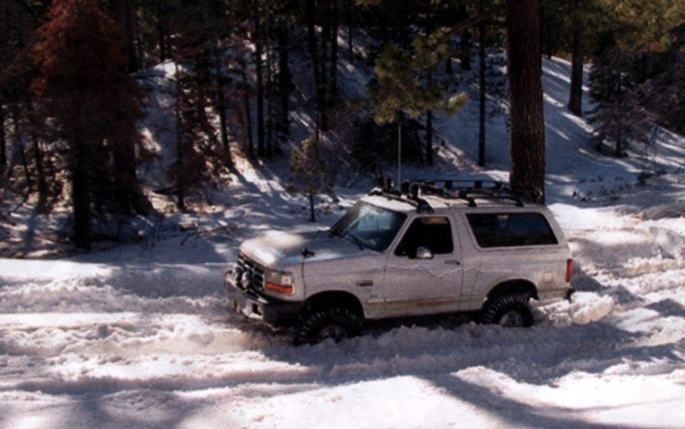 White SUV stuck in snow, 3/4 front view. Visible text 'SUPERMOTORS'