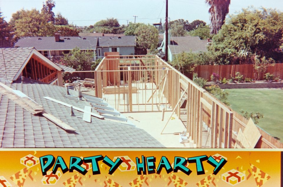 house construction with framing visible on roof and addition, backyard and neighboring houses in background