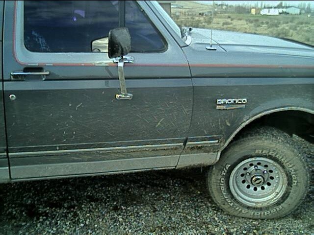 Mud-splattered driver side of a gray Ford Bronco with BFGoodrich all-terrain tire