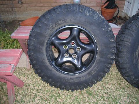 1999 Land Rover Discovery II - A spare tire with a black 5-spoke wheel sits on the grass next to a red wooden bench.