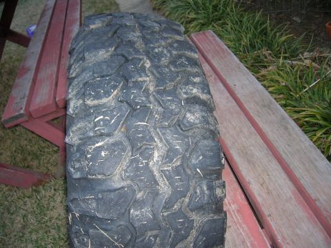 1999 Land Rover Discovery II - A single off-road tire with deep treads is shown resting on weathered red wooden planks outdoors.