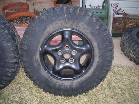 1999 Land Rover Discovery II - Close-up of a black five-spoke wheel mounted on an off-road tire.
