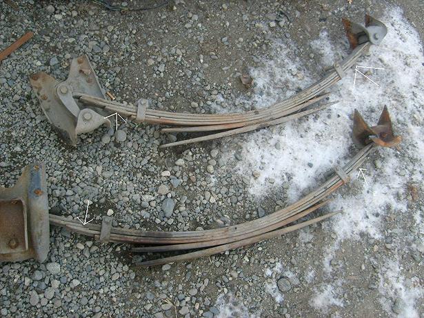 two sets of old leaf springs lying on gravel and snow