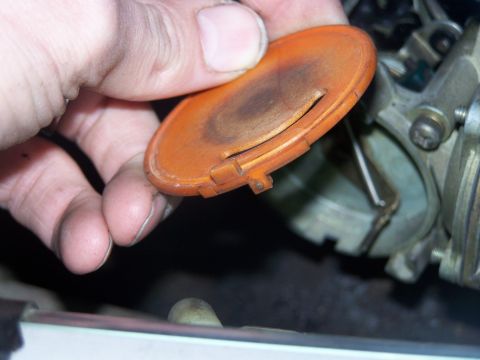 1986 Ford Bronco - A hand removes an orange choke cover from a vehicle's carburetor, revealing internal components.