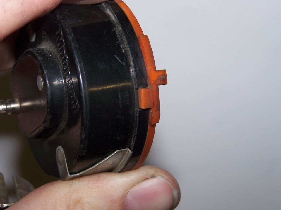 Close-up of a black and orange carburetor choke housing held by fingers