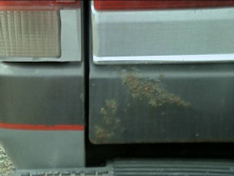 1989 Ford Bronco - Close-up of the driver's-side lower corner of a tailgate and the adjacent rear quarter panel, showing red and silver body stripes and a lar…