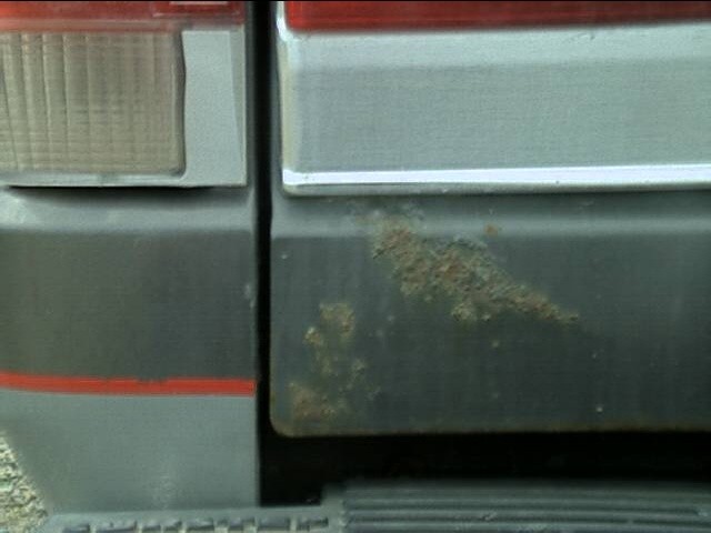 Rust bubbling along the lower driver-side corner of a striped gray tailgate