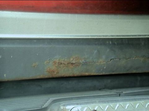 1989 Ford Bronco - Tight close-up of the lower center of a tailgate showing a horizontal split in the paint with heavy orange rust blistering along the bottom…